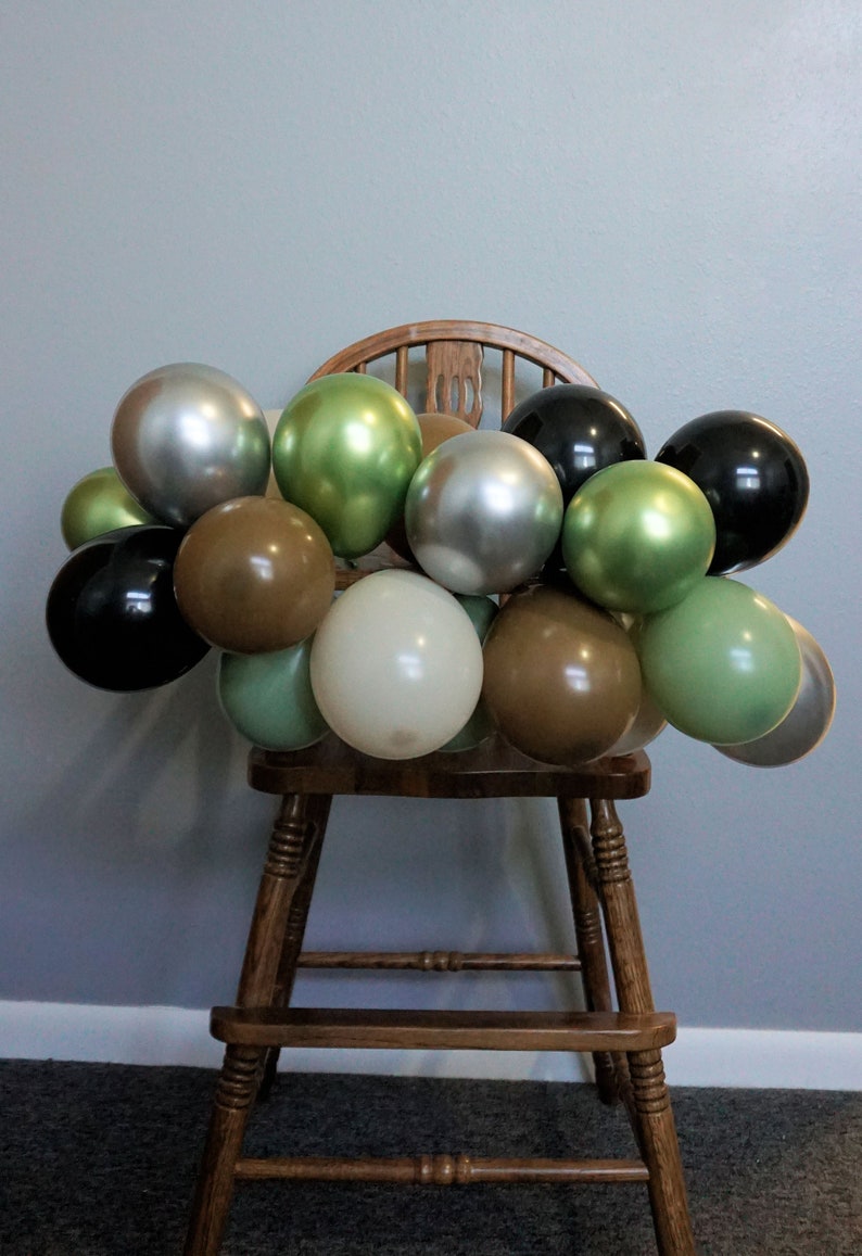 May include: A wooden chair decorated with a garland of balloons in various colours, including black, silver, green, brown, and cream.
