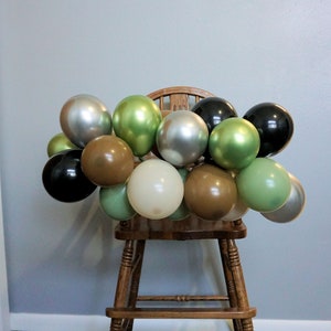 May include: A wooden high chair decorated with a garland of green, brown, silver, and black balloons.