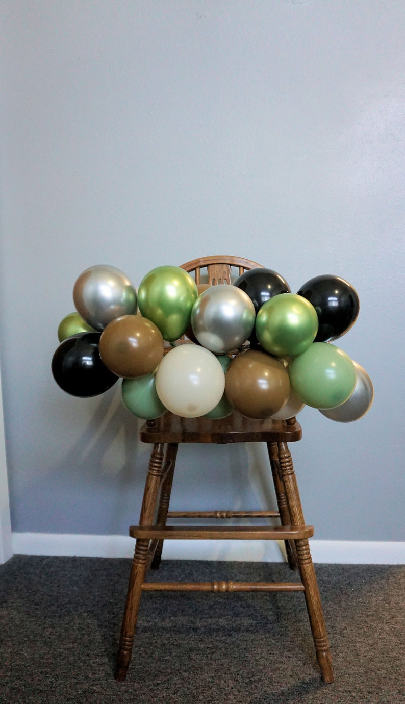May include: A wooden high chair decorated with a garland of green, brown, silver, and black balloons.