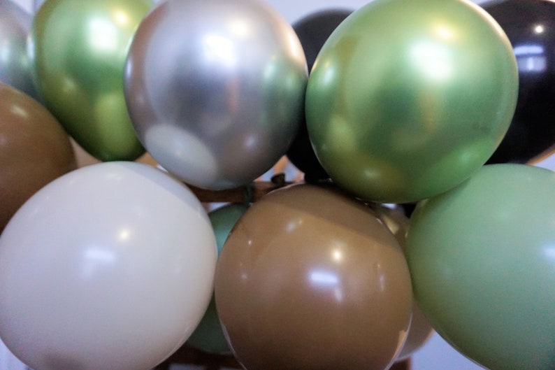 May include: A cluster of balloons in a variety of colours, including green, silver, brown, and white. The balloons are arranged with some overlapping.