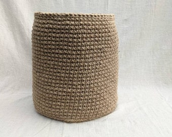 May include: A large, cylindrical, natural-fiber basket made of woven jute. The basket is a light brown color and has a smooth, even texture.