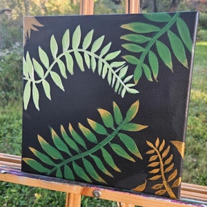 May include: A black canvas painting featuring green and gold fern leaves. The leaves are painted in a stylised, abstract manner.