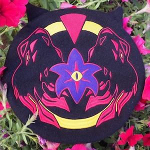 May include: Black felt beret with a red, yellow and purple embroidered design. The design features two stylised animal heads facing each other with a flower in the centre.