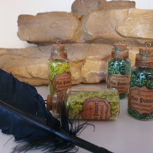 Könnte beinhalten: Vier kleine Glasflaschen gefüllt mit grünem Glitter und mit "Floo Powder" beschriftet, mit braunem Garn um den Hals jeder Flasche gebunden. Die Flaschen stehen auf einer felsigen Oberfläche.
