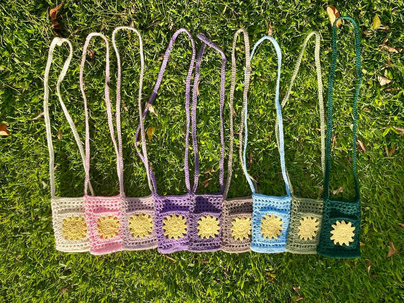 Op de afbeelding: Acht gehaakte mini-tasjes met verstelbare bandjes. Elk tasje heeft een andere kleur en een geel bloemenontwerp.