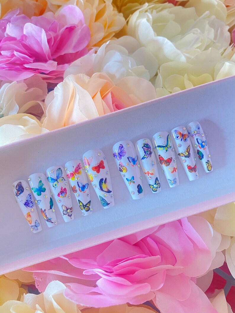 May include: A set of ten white false nails with colourful butterfly designs and rhinestones.