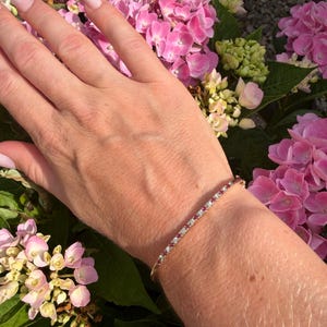 May include: A thin gold bangle bracelet featuring an alternating pattern of small, round, clear white stones and vibrant red stones set along the entire visible length of the band, creating a delicate and continuous line of sparkle on the wrist.