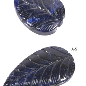 Puede incluir: Dos tallas de piedras preciosas de color azul oscuro con forma de hoja, etiquetadas como A-6 y A-5. Las piedras presentan vetas talladas y una superficie lisa y reflectante. La pieza superior es redondeada, mientras que la inferior es alargada y puntiaguda.