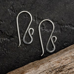 May include: A pair of silver earring hooks with a unique, twisted design. The hooks are made of metal and have a smooth, polished finish.