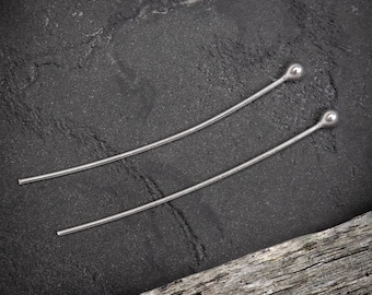 May include: Two silver hair pins with rounded ends. The pins are lying on a dark gray textured surface.