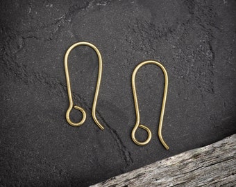 May include: Two gold-colored earring hooks on a dark gray background. The hooks are made of metal and have a simple design.