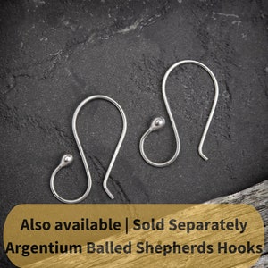 May include: Two silver ball ended shepherd's hooks, also known as French hooks, are shown on a dark gray textured surface.  Also available | Sold Separately Argentium Balled Shepherds Hooks