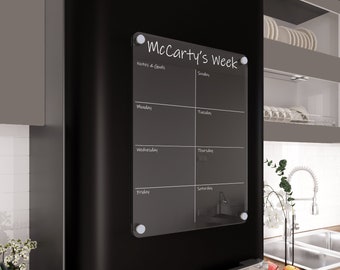 May include: A clear glass dry-erase weekly planner with the text "McCarty's Week" at the top. The planner is divided into seven sections for each day of the week, with the days labeled "Sunday", "Monday", "Tuesday", "Wednesday", "Thursday", "Friday", and "Saturday". The top section is labeled "Notes & Goals".