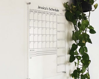 May include: A clear acrylic dry erase board with a monthly calendar, habit tracker, and notes section. The board has the title "Jessica's Schedule" and includes the months of the year.