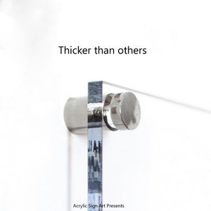 May include: Close-up of a clear acrylic sign with a silver metal stand. The sign is thicker than other signs. The text "Thicker than others" is printed above the sign. The text "Acrylic Sign Art Presents" is printed below the sign.