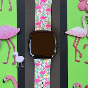 May include: A pink and white Apple Watch band with a flamingo print. The band is shown on a black and green background with pink flamingo cutouts.