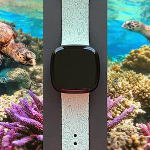 May include: A light green smartwatch band with a black screen. The band features a sea life pattern with shells, starfish, and turtles. The background shows a coral reef and sea turtles.