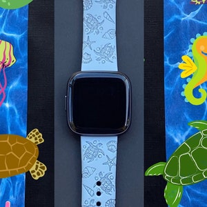 May include: A light blue silicone watch band with a sea life design. The band features sea turtles, seashells, starfish, and coral. The band is compatible with Apple Watch.