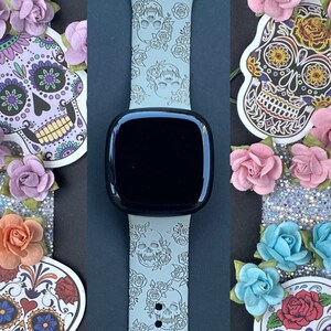 May include: A grey silicone watch band with a white and grey skull and flower pattern. The band is shown with four decorative sugar skull stickers.