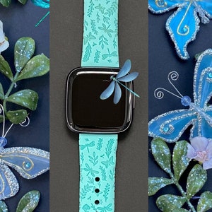 K&ouml;nnte beinhalten: Ein t&uuml;rkisfarbenes Silikon-Armband mit einem Libellen- und Blattmotiv. Das Armband ist auf einem schwarzen Hintergrund mit blauen Schmetterlingen und gr&uuml;nen Bl&auml;ttern abgebildet.