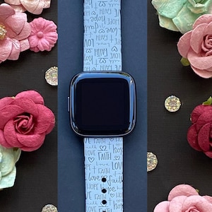 Puede incluir: Una correa de reloj de silicona azul claro con un patr&oacute;n repetido de las palabras "love", "faith" y "hope" en letras blancas. La correa est&aacute; dise&ntilde;ada para un reloj inteligente.