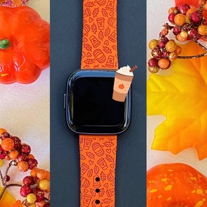 May include: Orange Apple Watch band with a fall-themed design featuring pumpkins, leaves, and coffee cups. The band is made of silicone and has a black background.
