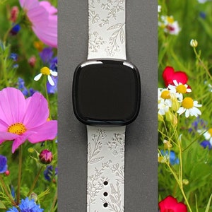 May include: White silicone watch band with a floral pattern. The band is shown on a black watch face and is surrounded by a field of wildflowers.