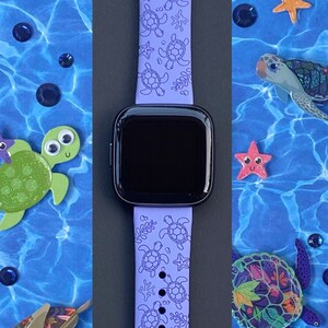 以下が含まれることがあります： 海ガメのデザインが施された紫色のシリコン製腕時計バンド。このバンドはスマートウォッチに対応しており、表面にテクスチャがあります。