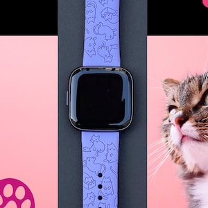 Pode incluir: Uma pulseira de rel&oacute;gio de silicone roxa com um padr&atilde;o de gatos. A pulseira &eacute; projetada para um smartwatch com uma face quadrada.