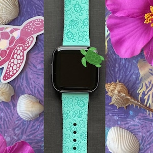 Pu&ograve; includere: Un cinturino per orologio in silicone blu turchese con un design a forma di tartaruga marina e conchiglie. Il cinturino &egrave; mostrato su uno sfondo nero.