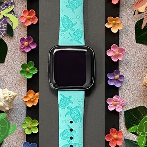 Op de afbeelding: Een lichtblauw siliconen horlogebandje met een herhalend patroon van zeeschildpadden. Het bandje is ontworpen voor een smartwatch en heeft een zwart scherm.