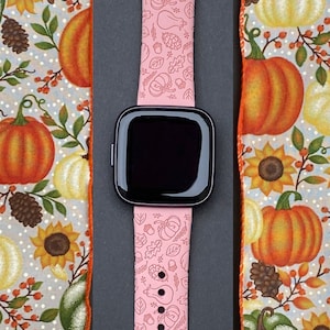 May include: A pink watch band with a fall-themed design featuring pumpkins, leaves, and acorns. The band is made of silicone and has a black watch face.