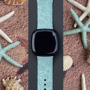 May include: A light blue Apple Watch band with a seashell and starfish pattern. The band is made of silicone and has a black watch face.