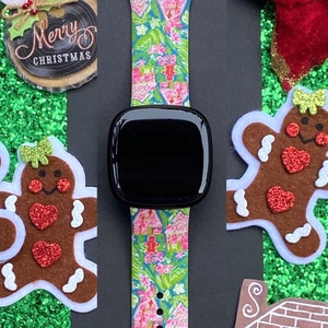 Op de afbeelding: Een kleurrijk kerstthema-horlogebandje met een gingerbreadhuis-patroon. Het bandje is gemaakt van siliconen en compatibel met de meeste smartwatches. Het bandje wordt getoond op een zwarte achtergrond met gingerbreadkoekjes en pepermuntstokken.