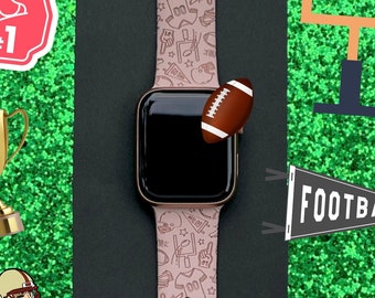 May include: A pink Apple Watch band with a football-themed design. The band features a variety of football-related icons, including helmets, footballs, and goalposts. The band is shown on a green background with a football and a goalpost.
