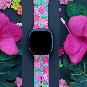 Op de afbeelding: Een horlogeband met bloemenprint met roze en groene bloemen op een turquoise achtergrond. De band is gemaakt van siliconen en heeft een zwart horlogeglas.