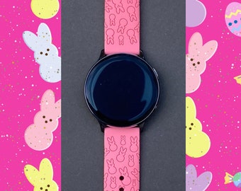 May include: Pink silicone watch band with a pattern of pastel pink bunnies. The band is compatible with a smartwatch with a black face.