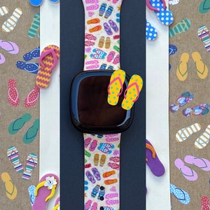 May include: A white Apple Watch band with a colorful flip-flop pattern. The band is made of silicone and has a black watch face.