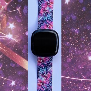 May include: A black smartwatch with a colorful firework print silicone band. The band has a pink, blue, and white firework design.