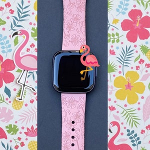 May include: Pink Apple Watch band with a tropical flamingo print. The band is made of silicone and has a black buckle.