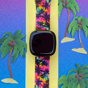 May include: A black smartwatch with a colorful tropical print band featuring palm trees and a sunset gradient. The band has silver accents.