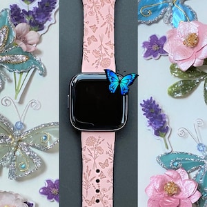 May include: A pink Apple Watch band with a floral design. The band is decorated with small butterflies and flowers. The watch face is black and shows the time.