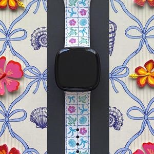 Op de afbeelding: Witte smartwatchband met een tropisch patroon van schildpadden, bloemen en schelpen. De band staat tegen een achtergrond met een herhalend patroon van blauwe strikken en schelpen, en is omgeven door kleurrijke bloemdecoraties.