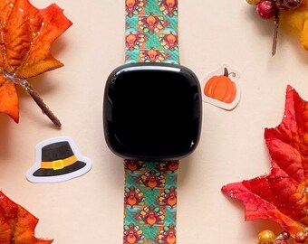 Puede incluir: Una correa de reloj con estampado de color turquesa y naranja con una esfera negra. La correa presenta un patrón repetitivo de pavos con sombreros de peregrino. El reloj está rodeado de decoraciones de otoño, incluyendo hojas, calabazas y bayas.