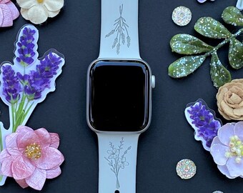 May include: White Apple Watch with a floral design on the band. The watch is surrounded by pink, white, and purple flowers.