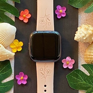 May include: A pink silicone watch band with a floral design. The band has a black watch face and is surrounded by seashells and flowers.
