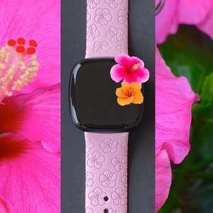 May include: A pink silicone watch strap with a floral pattern. The strap is designed for a smartwatch and has a black screen.