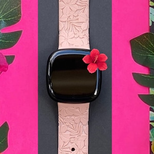 Puede incluir: Una correa de reloj de silicona rosa con un patr&oacute;n floral. La correa est&aacute; dise&ntilde;ada para un reloj inteligente y tiene una esfera negra.