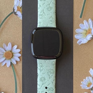 May include: A light green watch band with a floral pattern. The band is made of silicone and has a black watch face.