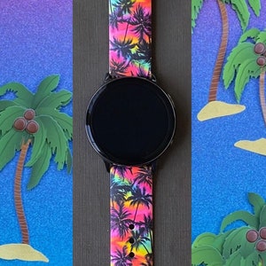 May include: A black smartwatch with a bright pink, yellow, and blue tropical palm tree print silicone band. The watch face is black and circular.